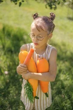 A funny child eats fresh carrots, holding zucchini in hands Stock Photos