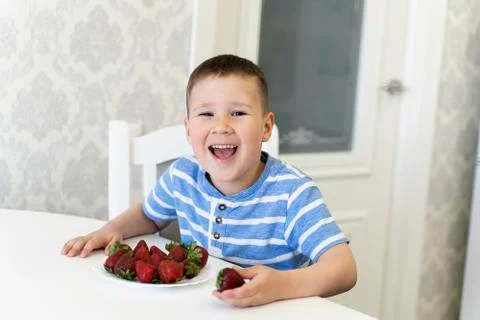 Funny child laughs and eats strawberries. spring. April-may. Stock Photos