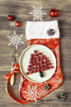 Funny Christmas tree shaped raspberry berry on plate, red sock on wooden back Stock Photos
