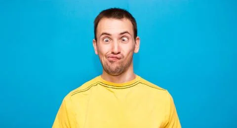 Funny comic man makes grimace with crosses eyes. Young man in yellow t-shirt  Stock Photos