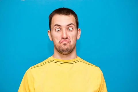 Funny comic man makes grimace with crosses eyes. Young man in yellow t-shirt  Stock Photos