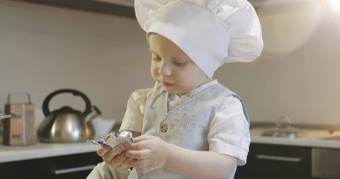 A funny cook child is sitting on a table and eating a chocolate candy. Stock Footage 85816071