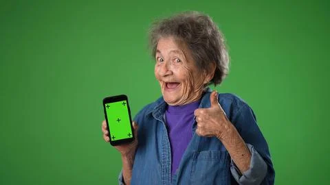 Funny crazy elderly old toothless woman points to phone with green screen Stock Photos