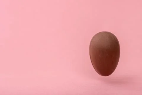 Funny creative concept of flying chocolate egg over pink background, copy spa Stock Photos