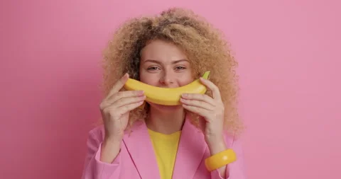 Funny curly haired young pretty European woman keeps yellow ripe banana near Stock Footage 154774276