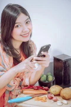 Funny cute asian girl with a mobile phone in her hands while preparing food Stock Photos