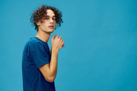 Funny cute curly tanned Caucasian guy in basic t-shirt folds hands looks at Stock Photos