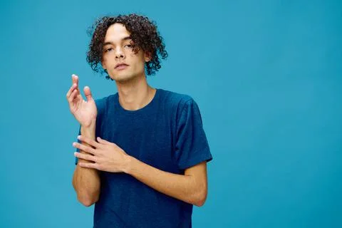 Funny cute curly tanned Caucasian guy in basic t-shirt folds hands looks at Stock Photos