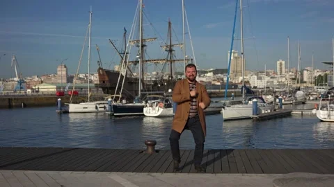 Funny dances of a man with a beard in sunny weather near the yacht on the pier Stock Footage 221804479