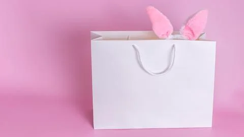 Funny Easter bunny ears in a white paper bag on a pink background. Stock Photos