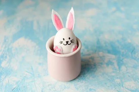 Funny Easter bunny made from egg placed in the pink cup on the blue background. Stock Photos