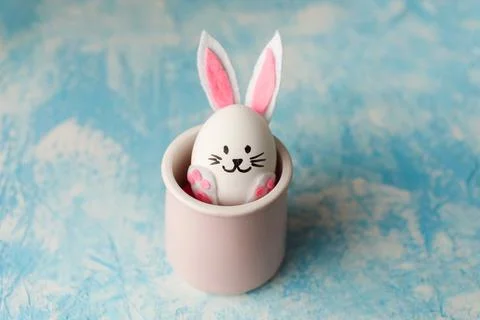 Funny Easter bunny made from egg placed in the pink cup on the blue background. Stock Photos