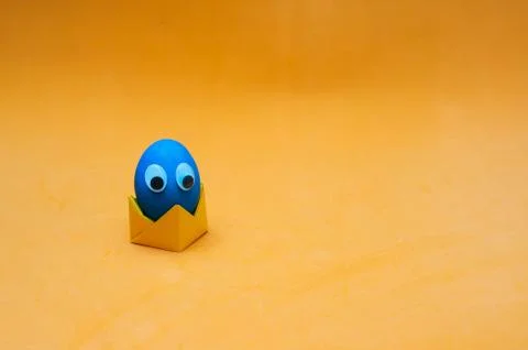 Funny easter egg with googly eyes on paper origami stand. Easter concept. Pla Stock Photos