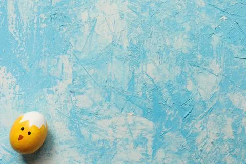 Funny Easter egg painted as chick on light blue textured background. Copy space. Stock Photos