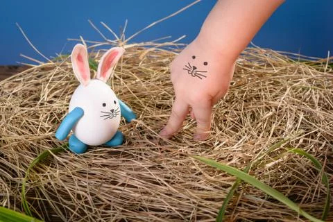 Funny easter rabbit and child hand with cute face. Nest from dry grass with.. Stock Photos