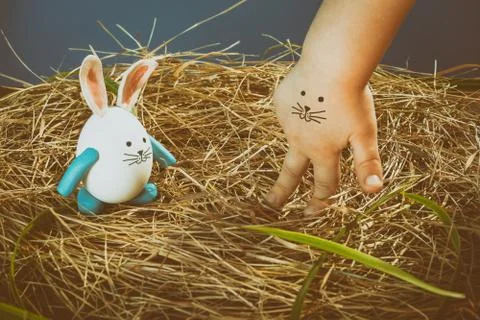 Funny easter rabbit and child hand with cute face. Nest from dry grass with.. Stock Photos