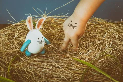 Funny easter rabbit and child hand with cute face. Nest from dry grass with.. Stock Photos