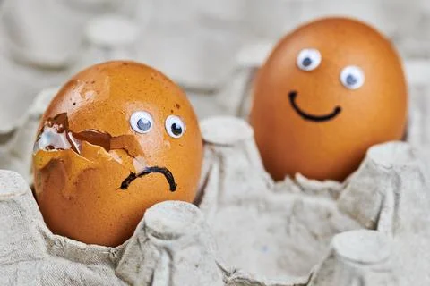 Funny egg and sad cracked egg in paper egg tray Stock Photos