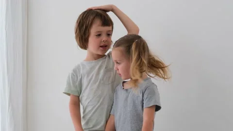 Funny elder boy measures height with younger girl at home Stock Footage 157467251