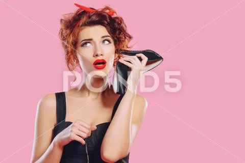 Funny expressive girl with high-heeled shoe in her hands. Pin-up style. Fashi Stock Photos