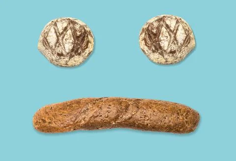Funny face made of bread buns and dark baguette on blue background. Stock Photos