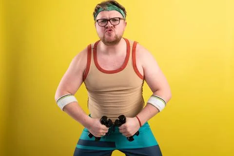 Funny fat man doing exercises with dumbbells. Overweight. yellow background Фото