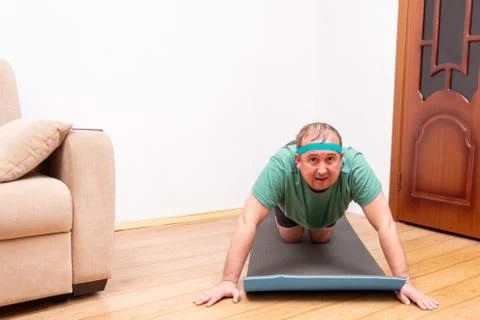 A funny fat man in a green bandana and t-shirt does push-UPS with a grimace o Stock Photos