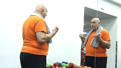 Funny fat man starting to pick up the smallest dumbbells Stock Footage 96670063