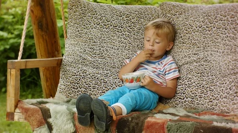 A funny four-year-old boy enjoys eating raspberries on a village swing. Stock Footage 129638353