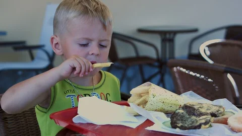 A funny four-year-old boy enjoys eating a burger in a cafe. Stock Footage 129639529