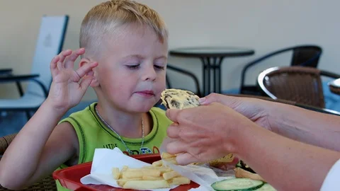 A funny four-year-old boy enjoys eating a burger in a cafe. Stock Footage 129639745
