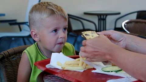 A funny four-year-old boy enjoys eating a burger in a cafe. Stock Footage 129640101