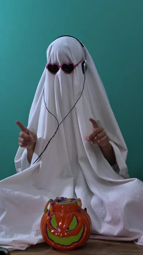 Funny ghost costume dancing with headphones by Halloween candy bucket 스톡 동영상 342521500