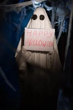 Funny ghost in dark corridor with cobweb showing board with happy halloween Stock-Fotos