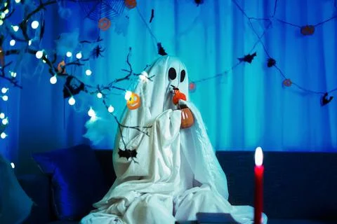 A funny ghost drinking from a pumpkin mug at home. Festive spooky decoratio.. Stock Photos