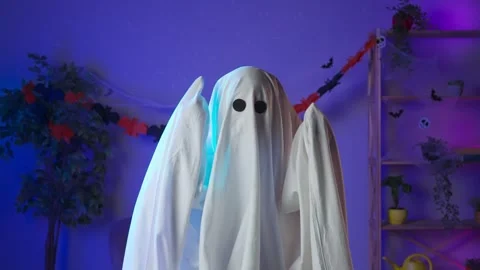 Funny ghost in a white sheet with black eyes in a dark room confusedly Stock Footage 285743548