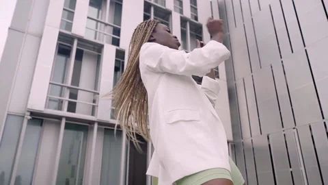 Funny girl performing cool dance opposite the modern building gray and green Stock Footage 207237775