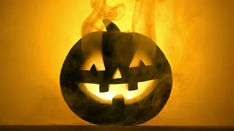 Funny glowing pumpkin Jack-o-lantern in the smoke on a orange background. 库存影片 137964055