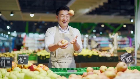 Funny greengrocer man throwing an apple at the workplace. A cheerful salesman in Stock Footage 199847970