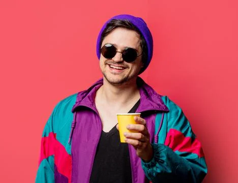 Funny guy in 80s style jacket and sunglasses holds paper cup on red backgorun Stock Photos
