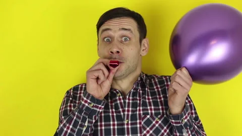 A funny guy actively plays with a purple balloon and blows in a party horn. Stock Footage 127646133