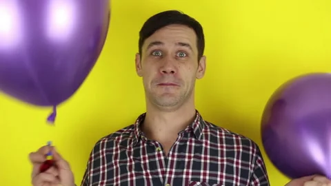A funny guy actively plays with a purple balloon and blows in a party horn. Stock Footage 127646458