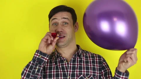 A funny guy actively plays with a purple balloon and blows in a party horn. Stock Footage 127646570