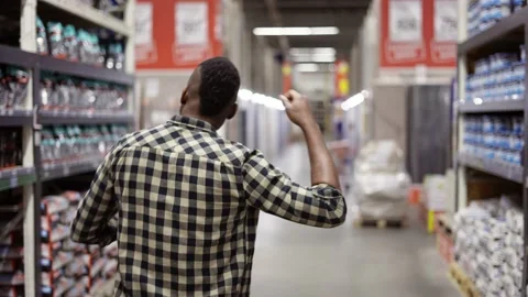 Funny guy dances gesturing in hardware goods store between stacks, rear view Video stock 171658139