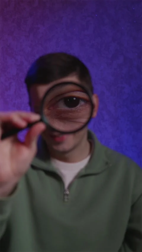 Funny guy laughing while looking through magnifying glass at camera Stock Footage 333757194