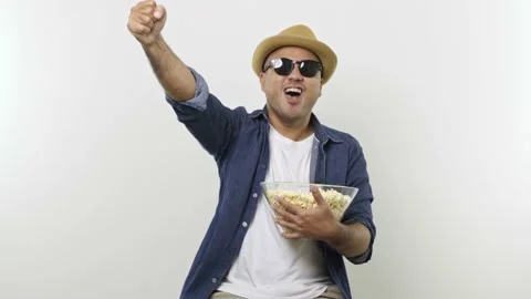 A funny guy in sunglasses eats popcorn while watching something action isolated  Stock Footage 144653440