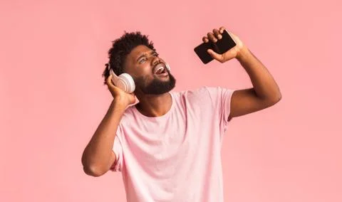 Funny guy with wireless headset singing over pink background Stock Photos