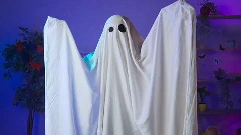 Funny halloween ghost in white sheet with black eyes in dark room pops up into Stock Footage 285741239