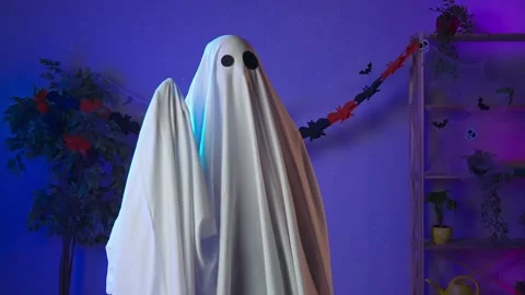 Funny halloween ghost in white sheet with black eyes in dark room standing and Stock Footage 285741305
