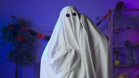Funny halloween ghost in white sheet with black eyes in dark room talking on Stock Footage 285742129